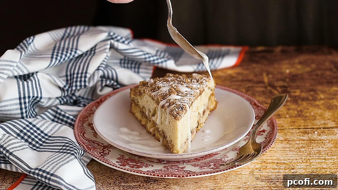 A delectable slice of fresh apple coffee cake is being adorned with a delicate drizzle of sweet icing, adding a finishing touch of elegance and flavor.