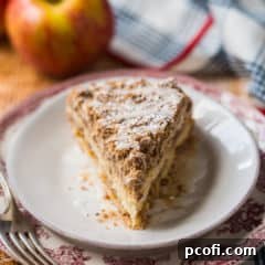 Slice of apple coffee cake on a red patterned plate, with fresh apples in the background.