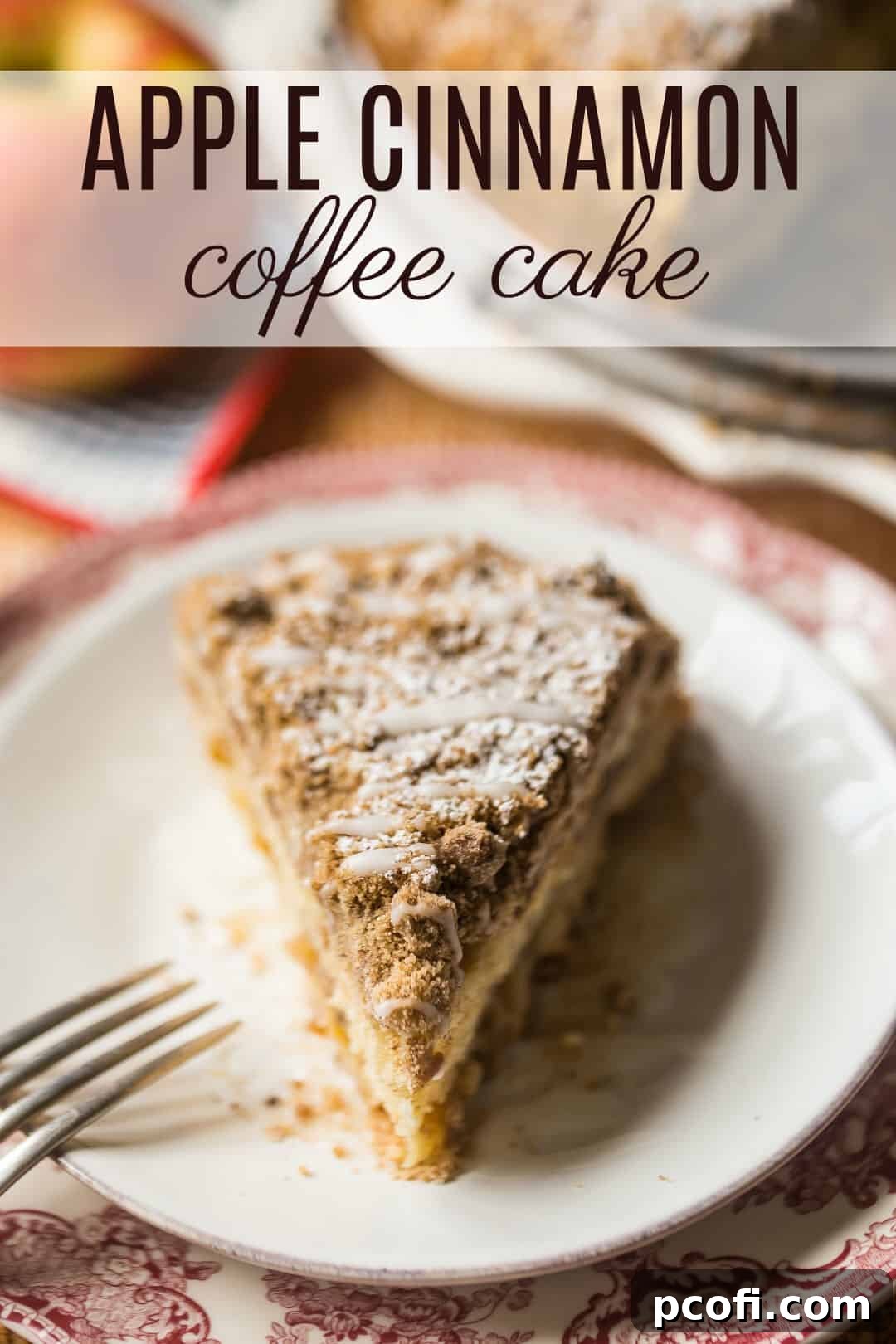 A triangular slice of the decadent apple coffee cake rests on a plate, with a rustic arrangement of fresh apples providing a beautiful, natural backdrop.
