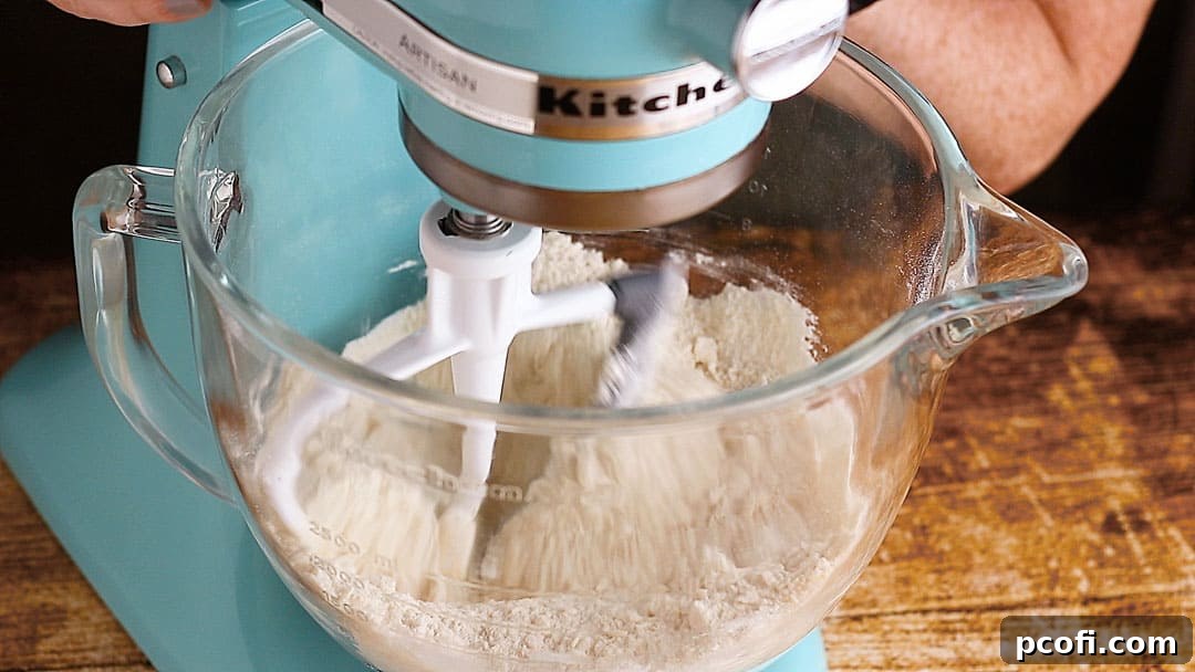 The softened butter is being mixed into the dry ingredients in a stand mixer, creating a crumbly, sand-like texture, characteristic of the reverse creaming method.