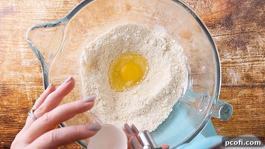 An egg is being added to the sour cream cake batter in a mixing bowl, gradually incorporating into the smooth mixture.
