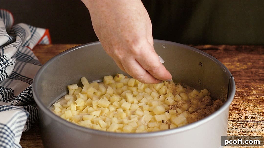 Cinnamon streusel is being artfully sprinkled over a layer of fresh apples within the coffee cake, adding a textured, spiced element.