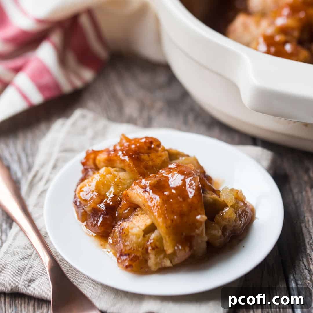 Two apple dumplings on a white plate with a copper fork and a linen napkin in the background. A classic fall dessert, perfect for homemade enjoyment.