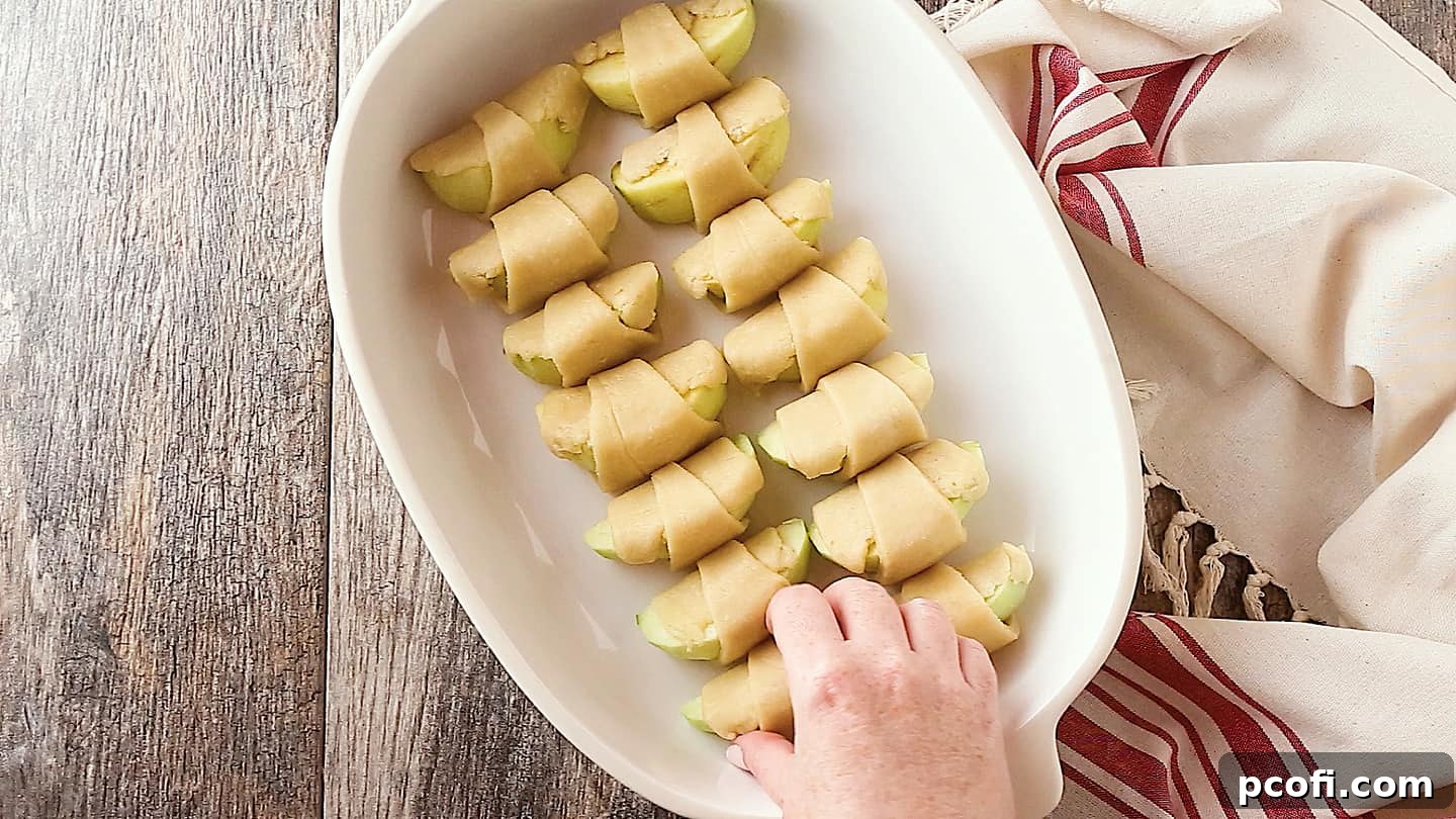 Placing apple dumplings in a casserole dish, preparing them for baking with the delicious sauce.