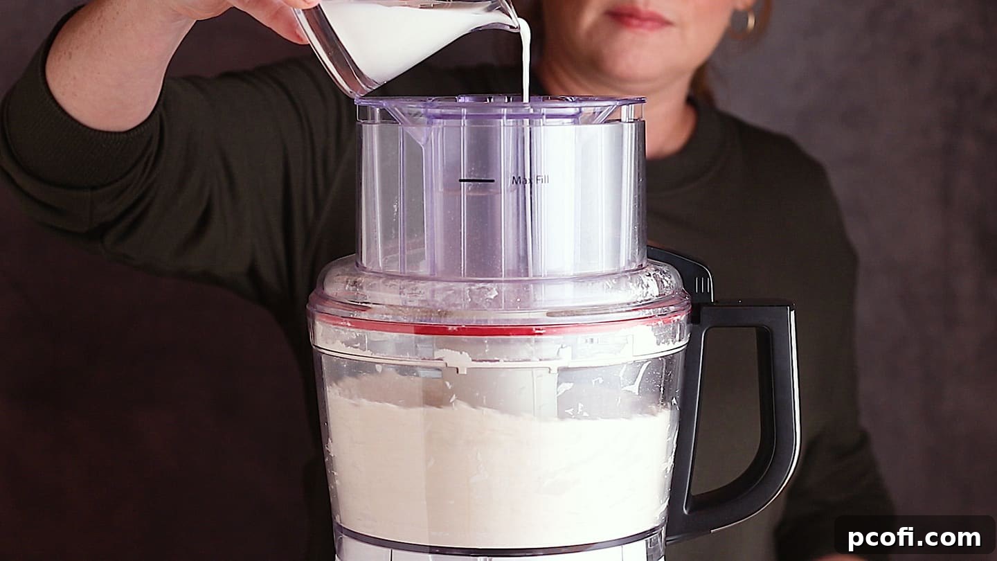 Drizzling cold milk into pastry dough for apple dumplings, ensuring proper hydration for a perfect crust.