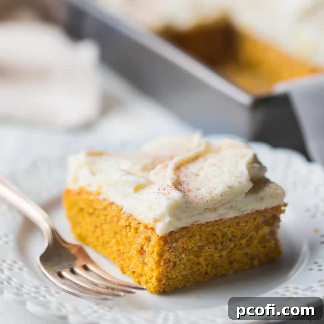 Square slice of pumpkin cake with cream cheese frosting and cinnamon on top, on a white background.