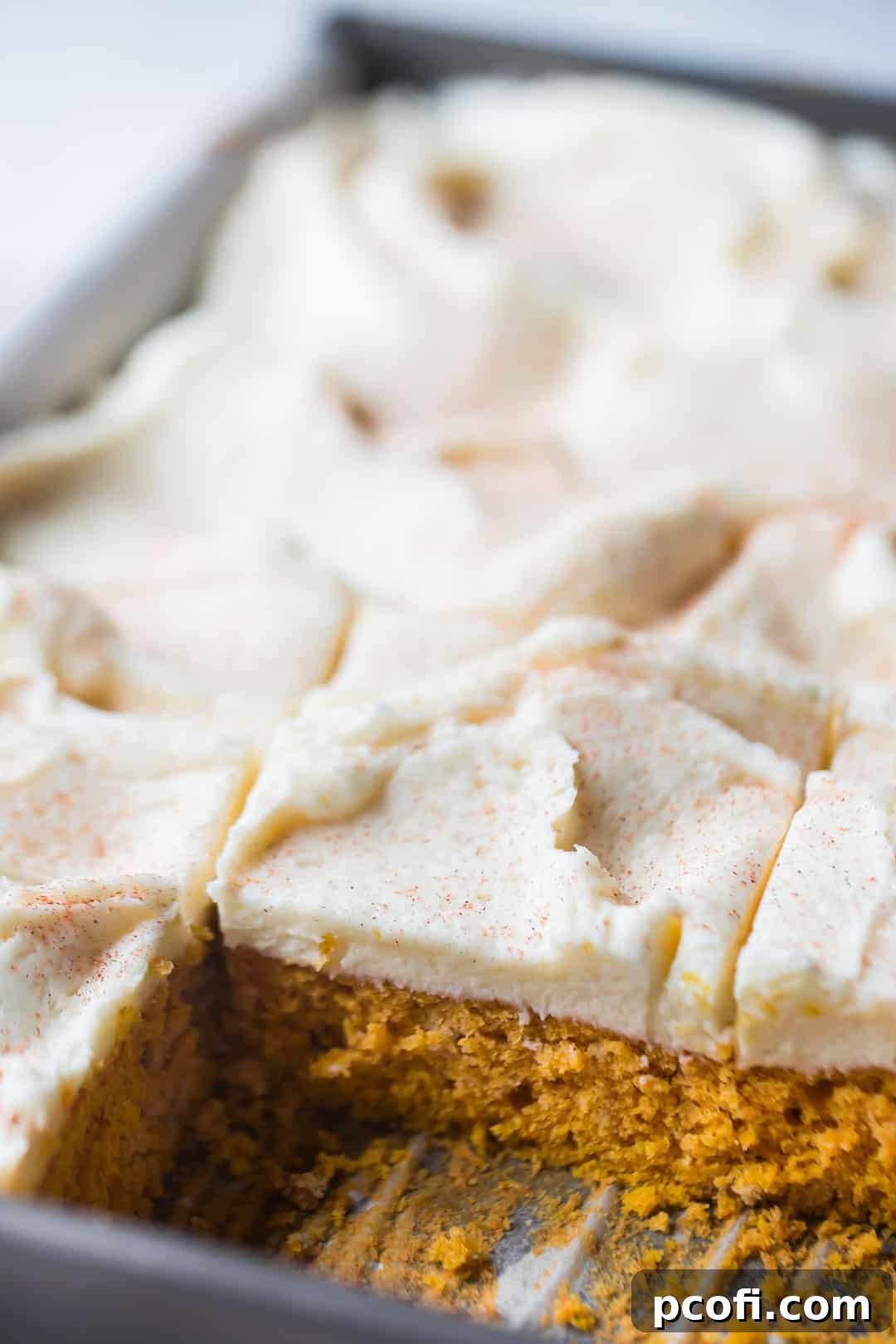 Rectangular pan of pumpkin spice cake with swirls of cream cheese frosting, on a pale background.