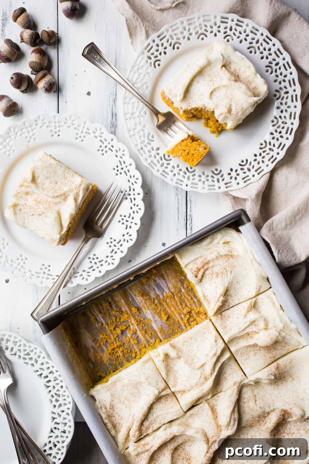 Overhead image of a pan of pumpkin cake, surrounded by plates of pumpkin cake with acorns and a linen napkin.