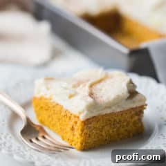 Square slice of pumpkin cake with cream cheese frosting and cinnamon on top, on a white background.
