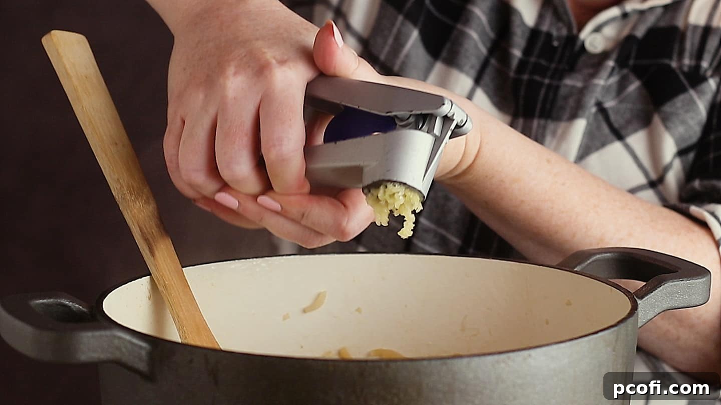 Pushing garlic through a garlic press and into a pot of French onion soup.