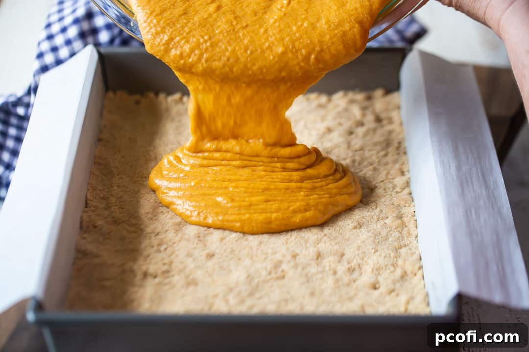 Pouring the smooth, spiced pumpkin gooey butter cake batter over the prepared crust in a 9x13-inch baking pan, ready for baking.