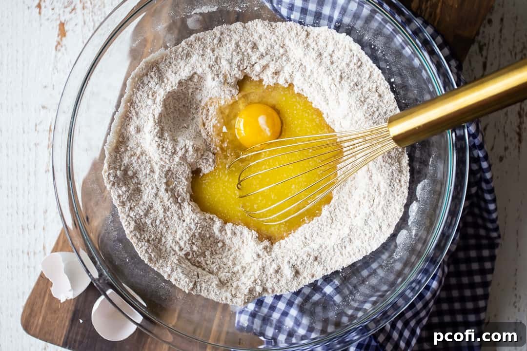 A large glass bowl containing the whisked dry ingredients for pumpkin gooey butter cake, alongside a separate bowl of eggs and melted butter, ready to be combined for the rich cake base.