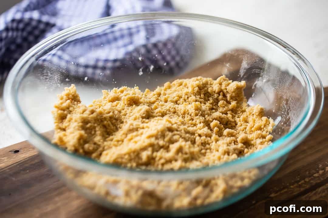 The combined base cake layer mixture for pumpkin gooey butter cake in a large glass mixing bowl, showcasing its crumbly, graham cracker-like texture before pressing into the pan.