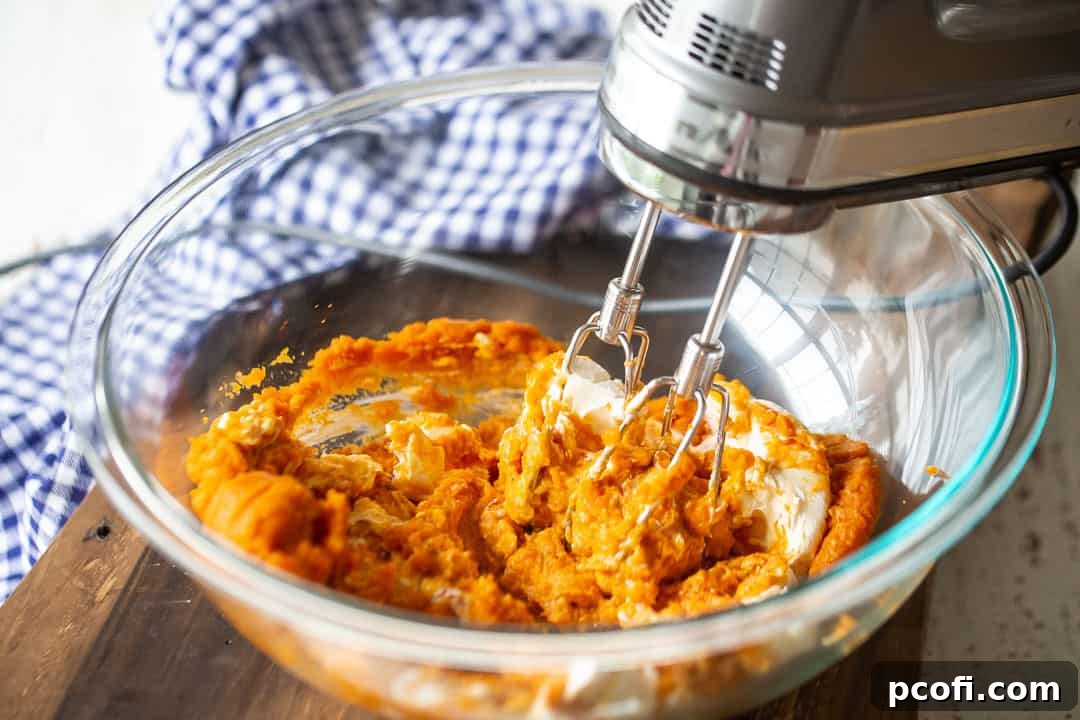 Mixing softened cream cheese and pumpkin puree in a large bowl, creating the smooth, creamy base for the pumpkin gooey butter cake filling.