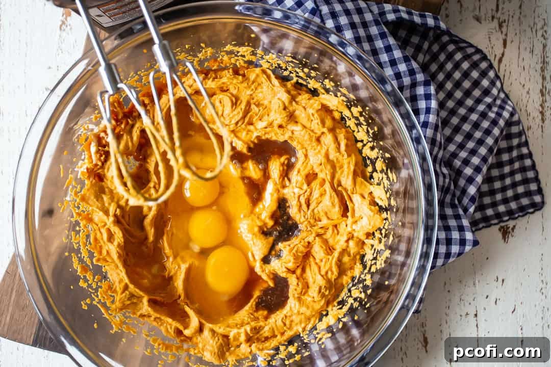 Adding eggs and vanilla extract to the pumpkin and cream cheese mixture, preparing for the next stage of the pumpkin gooey butter cake filling.