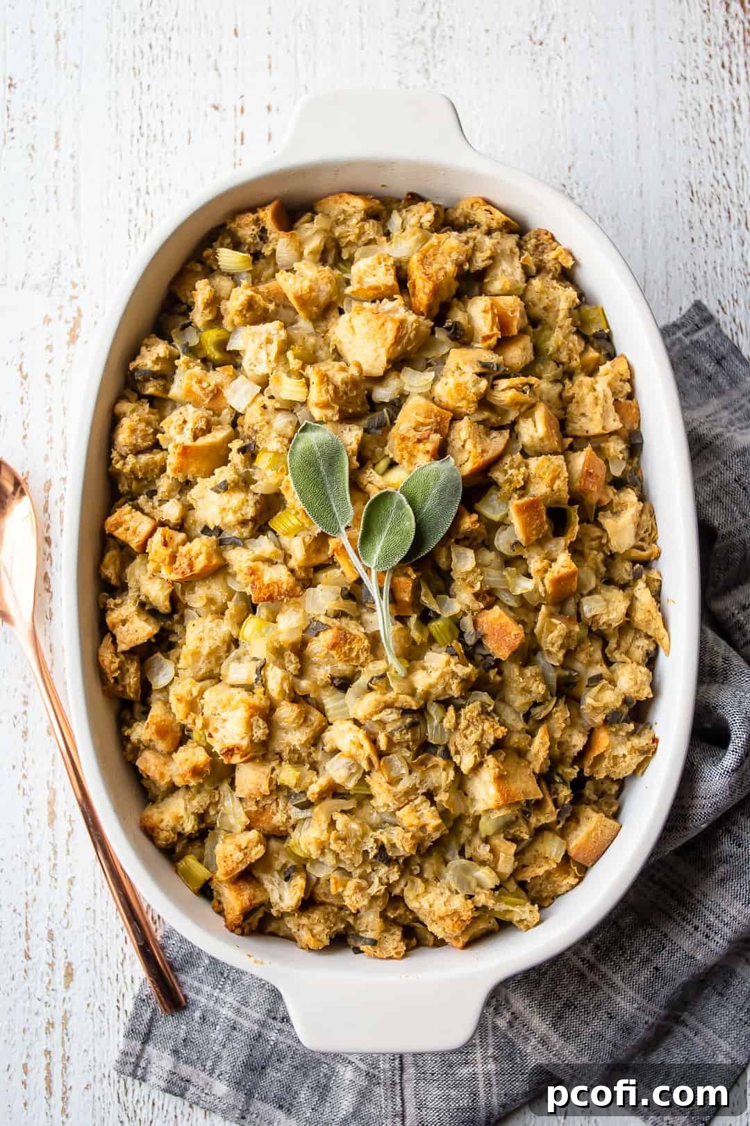 Overhead image of the best Thanksgiving stuffing recipe, baked in a white dish with a copper serving spoon.