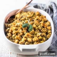 Thanksgiving stuffing recipe baked in a white casserole dish with fresh sage and a gray cloth in the background.