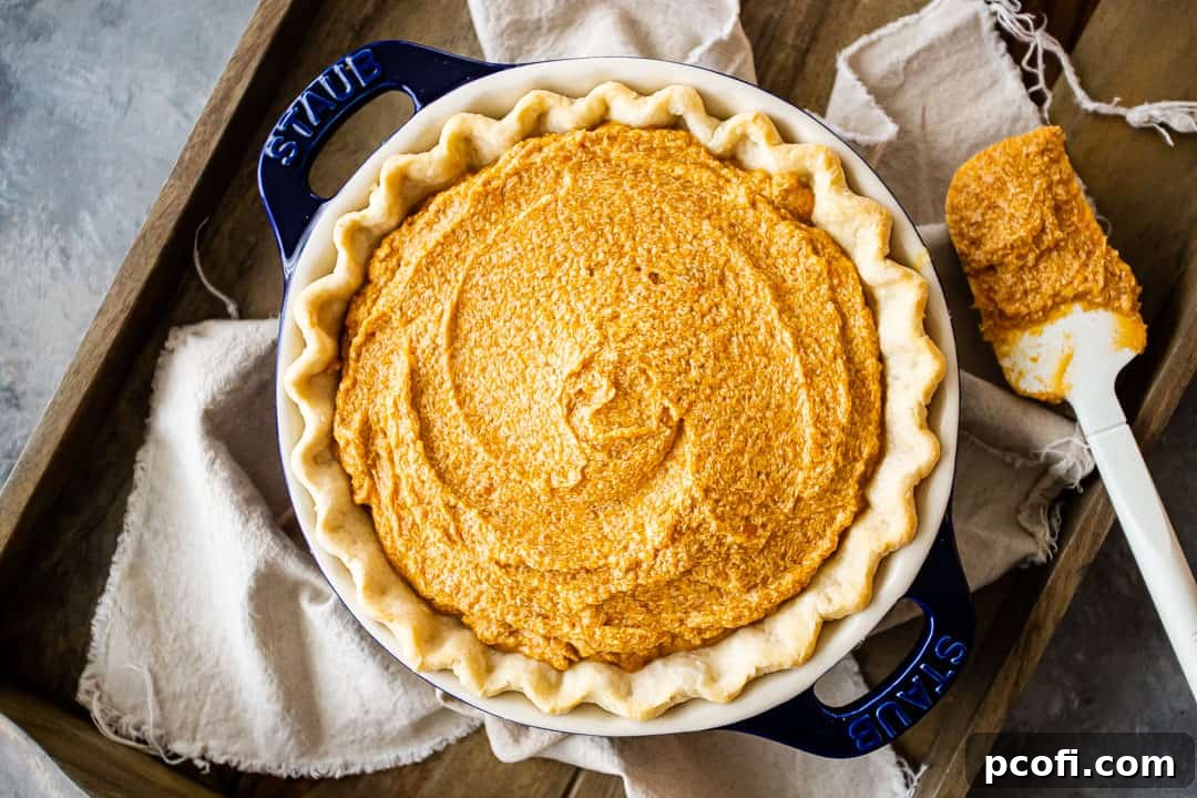 An unbaked sweet potato pie, nestled in its crust on a baking sheet, with a rustic linen cloth draped nearby, awaiting its transformation in the oven.