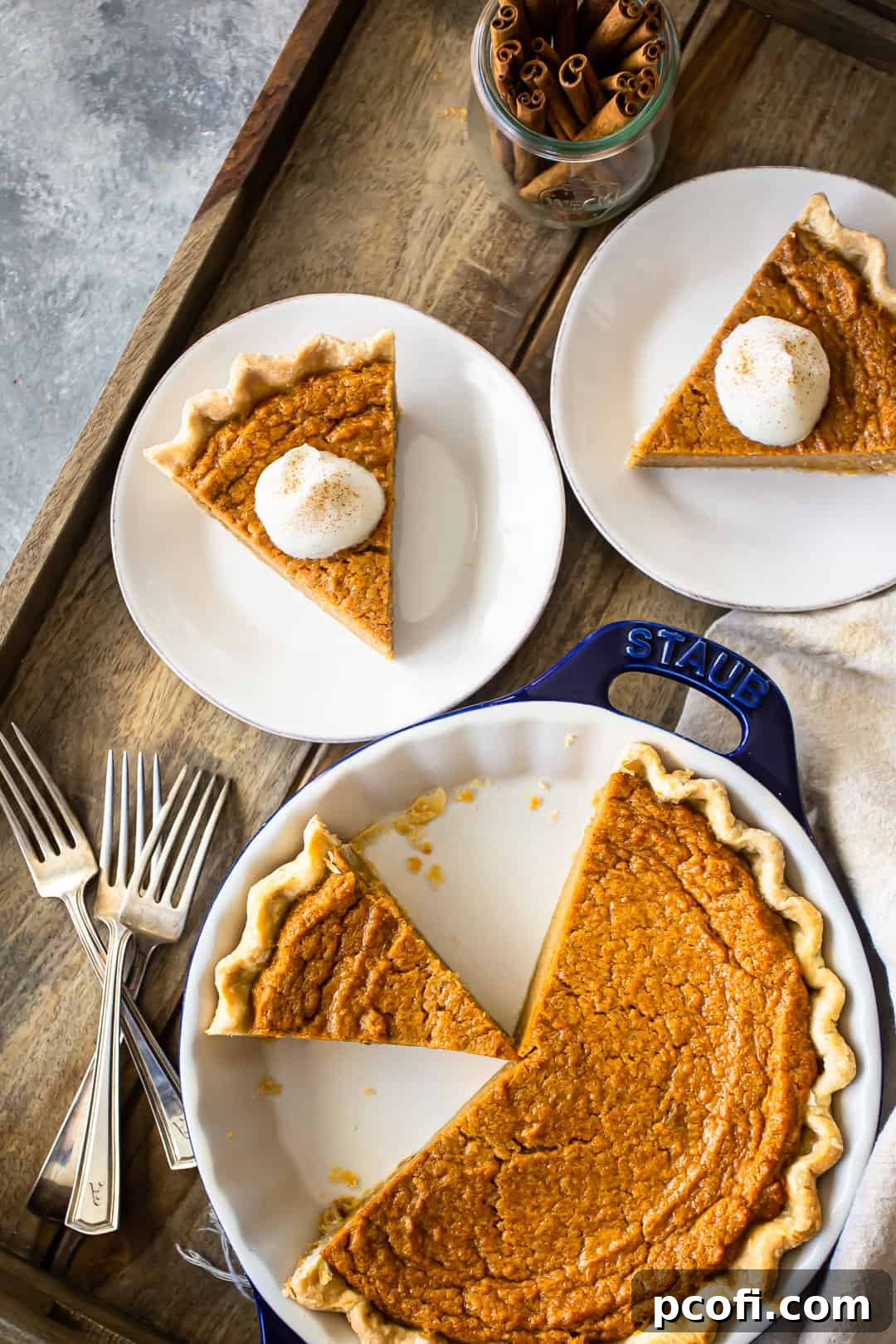 An inviting overhead view of a whole sweet potato pie, already sliced, presented on a rustic wooden tray with a scattering of serving plates in the background.