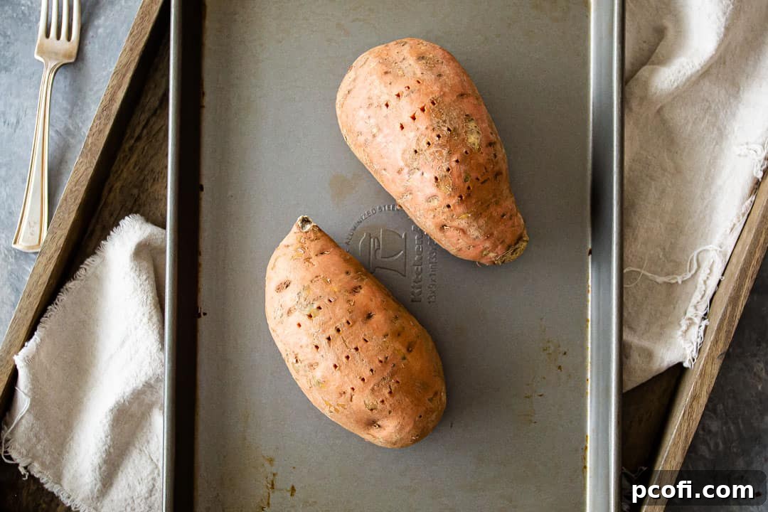 Two vibrant orange sweet potatoes neatly arranged on a baking sheet, ready for roasting to bring out their natural sweetness.