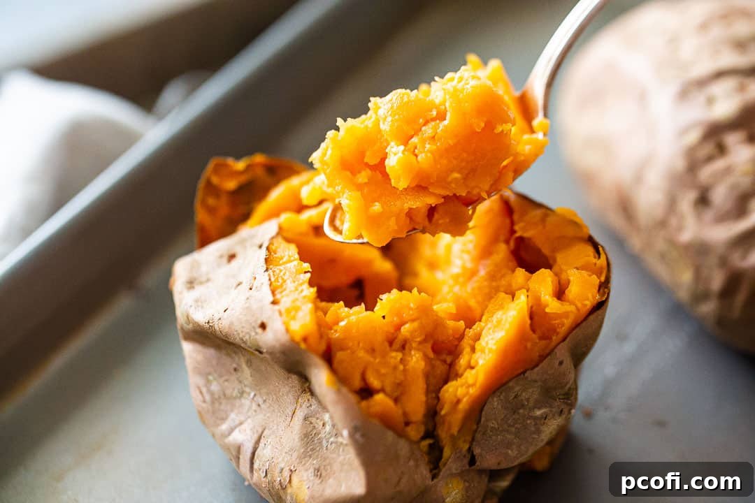 A spoon meticulously scooping the soft, cooked flesh from a perfectly roasted sweet potato into a glass mixing bowl, showcasing the rich orange color.