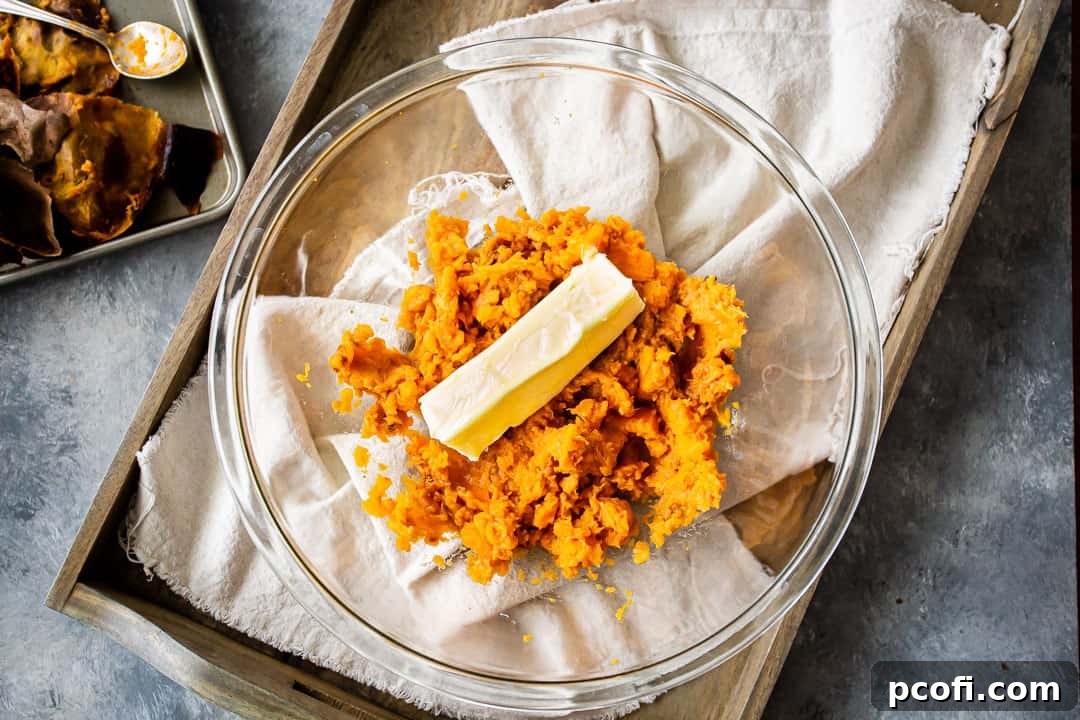 Creamy mashed roasted sweet potatoes and softened butter combined in a clear glass bowl, forming the luscious base for the sweet potato pie filling.