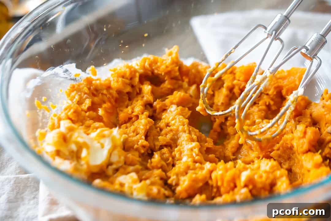 An electric mixer effortlessly mashing roasted sweet potatoes, incorporating softened butter into a smooth, creamy base for the pie filling.