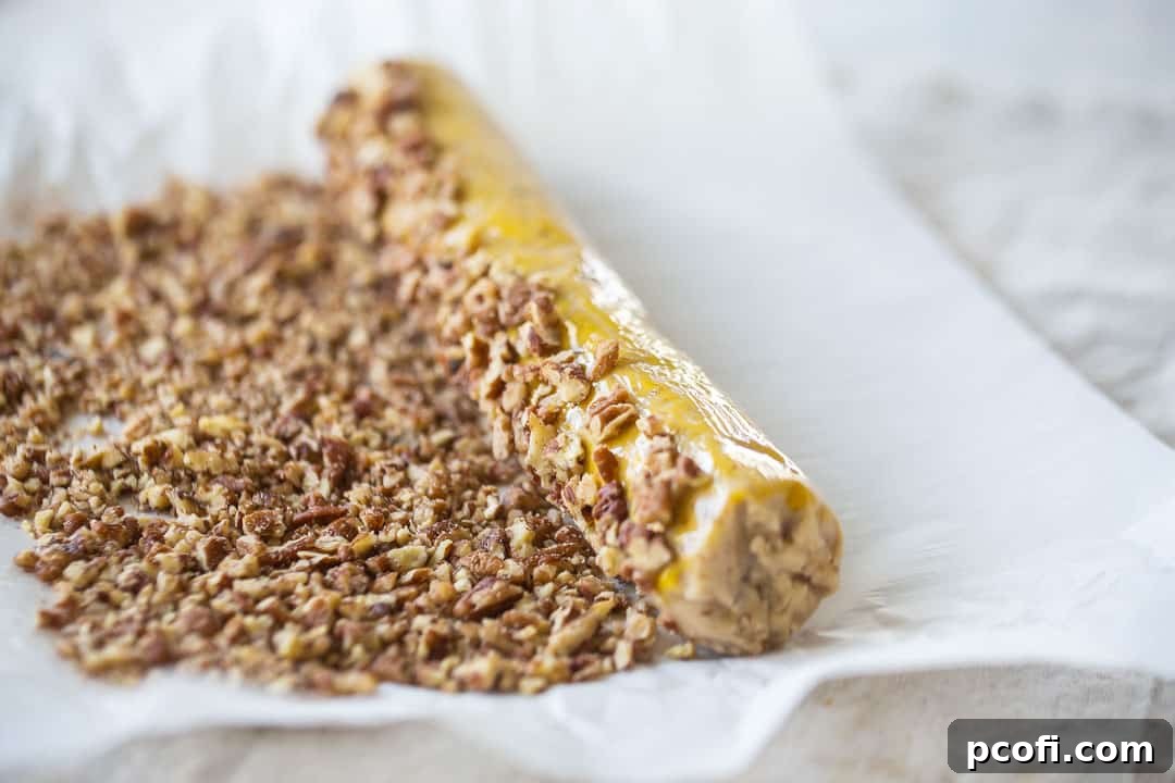 A pecan sandies dough log being rolled generously in chopped pecans, ensuring a full and delicious coating.