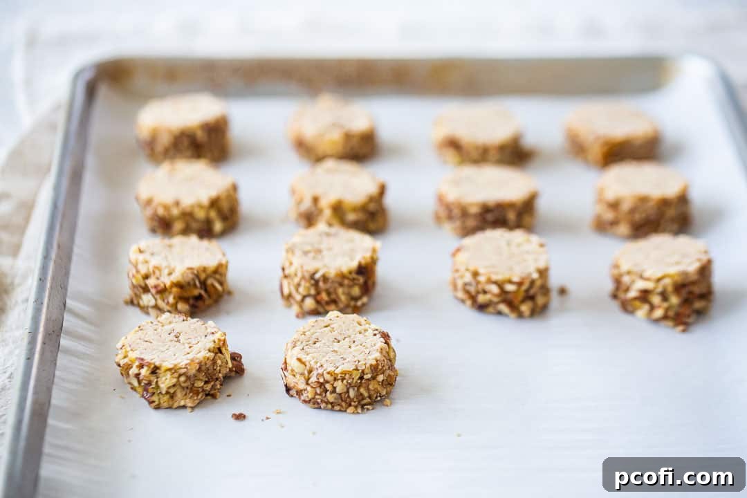 Unbaked pecan sandies cookies, perfectly sliced and arranged on a parchment-lined baking sheet, awaiting their turn in the oven.