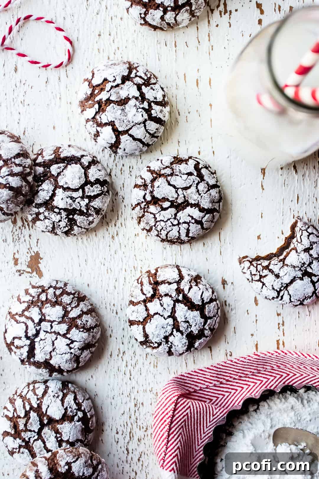 Baked crinkle cookies on a distressed white table with a red kitchen towel and a bottle of milk, ready to be enjoyed.