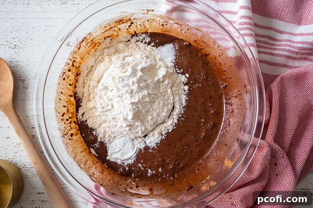 Adding flour to the chocolate crinkle cookie wet ingredients, illustrating the final step of dough preparation.