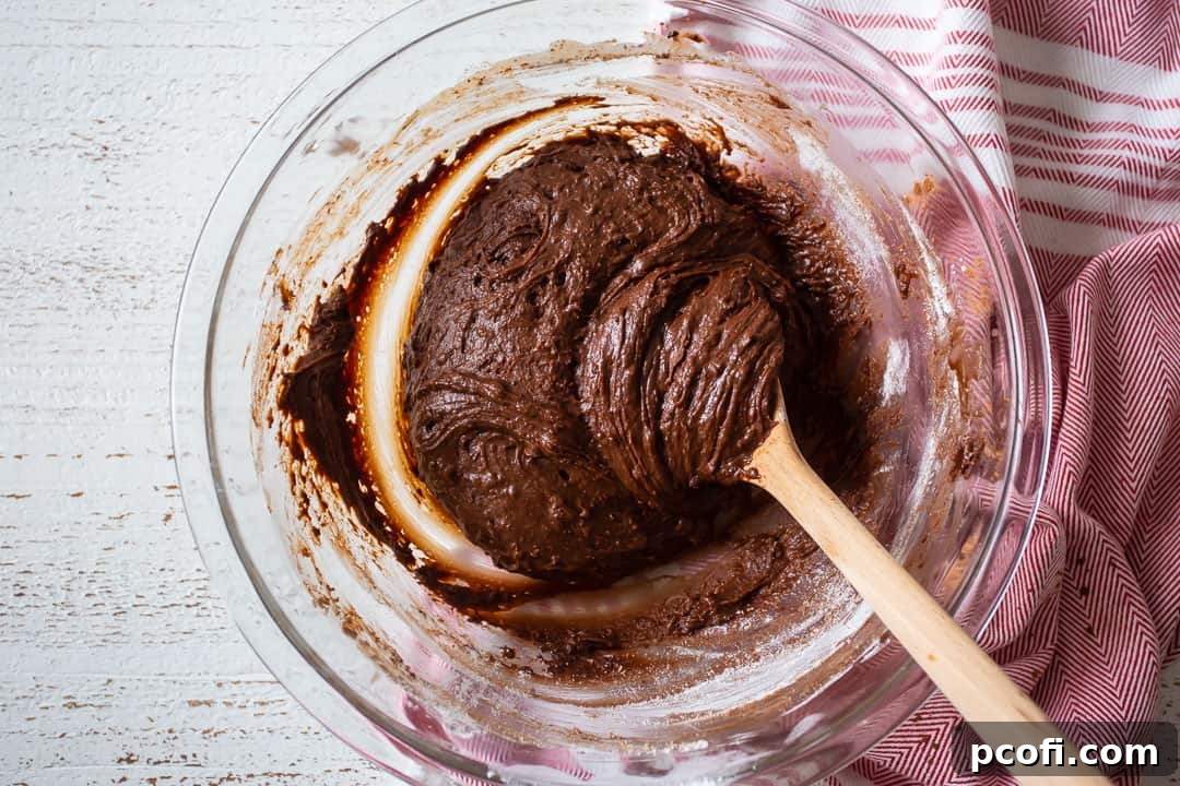 Chocolate crinkle cookie dough resting in a glass mixing bowl, demonstrating its ready-to-chill state.