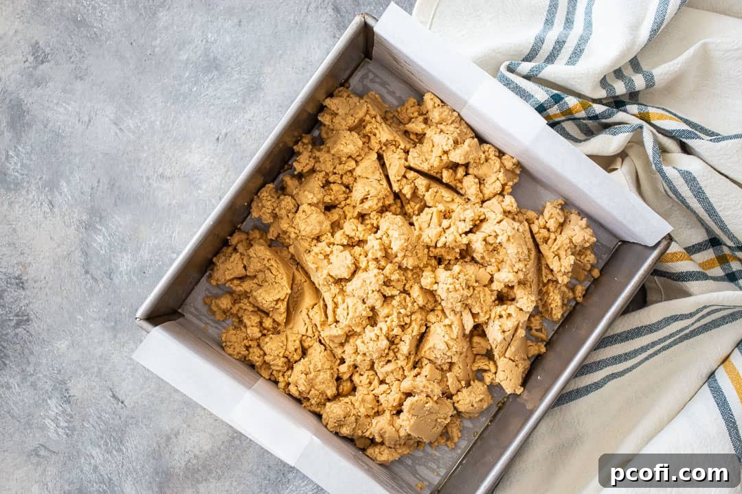 Smooth, warm peanut butter fudge mixture pressed evenly into a parchment-lined 8x8 inch pan.