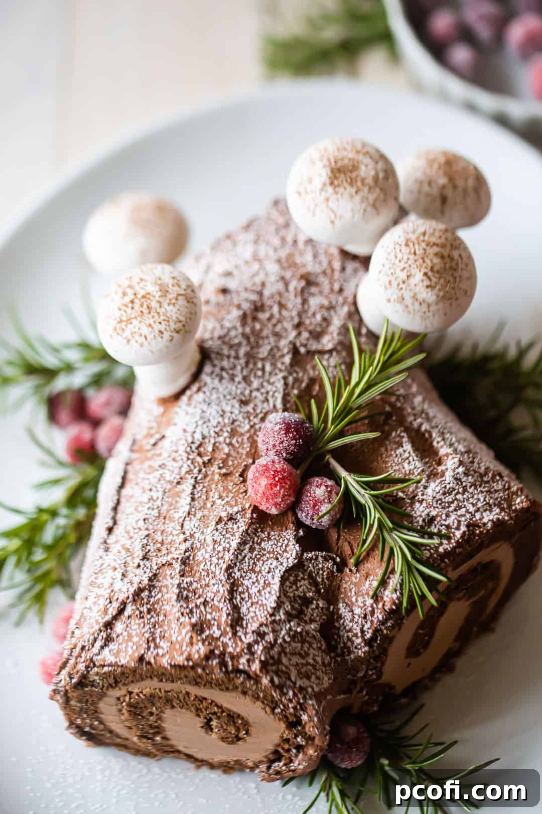 A fully prepared and beautifully garnished chocolate yule log cake, dusted with powdered sugar and adorned with charming meringue mushrooms, ready for a festive holiday celebration.