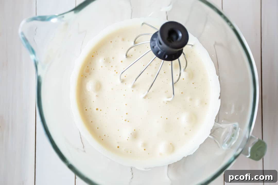 Whipping eggs with sugar in a stand mixer to create a light and airy base for a chocolate yule log cake.