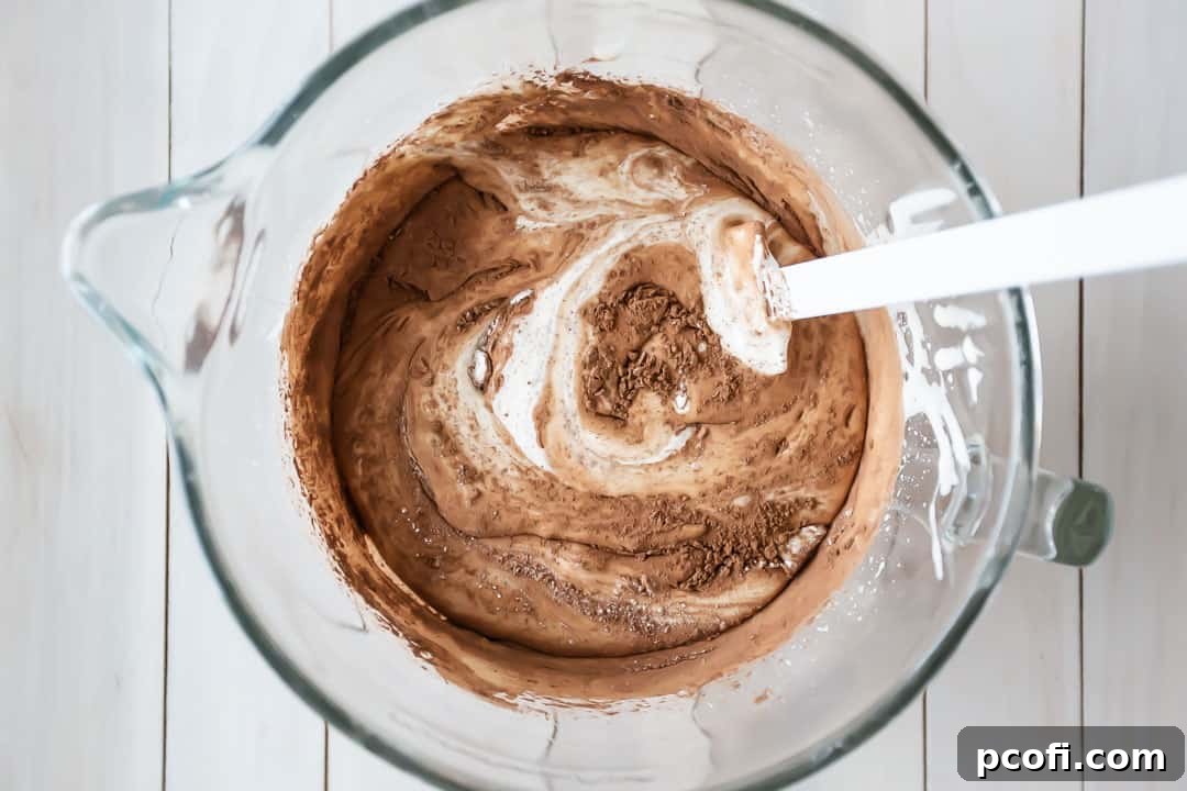 Carefully folding unsweetened cocoa powder and all-purpose flour into the whipped egg batter for a chocolate yule log cake, ensuring airiness.