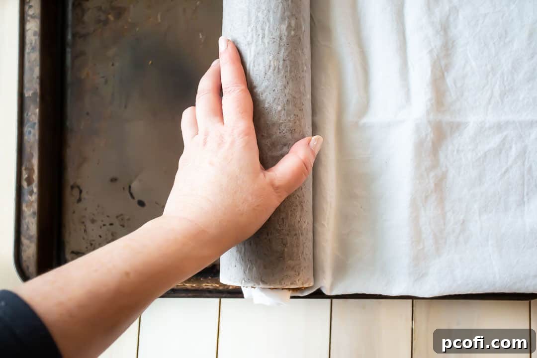 Carefully rolling a warm chocolate yule log cake with a clean kitchen towel, a technique to create the iconic spiral shape.