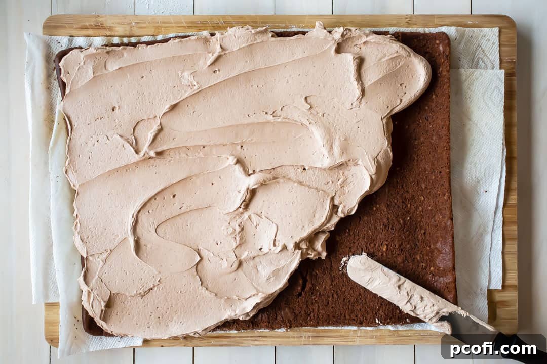 Spreading a generous layer of fluffy chocolate whipped cream filling onto an unrolled chocolate yule log cake, ready for re-rolling.