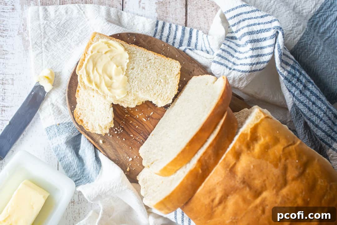Overhead view of several slices of homemade soft white sandwich bread artfully arranged on a wooden cutting board, accompanied by a small bowl of softened butter, emphasizing its readiness for serving.
