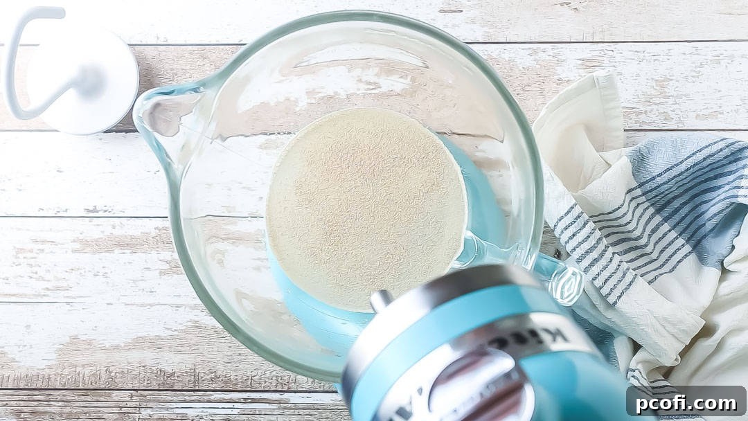 Close-up of active dry yeast dissolving and starting to foam in warm, sugary water within a large mixing bowl.
