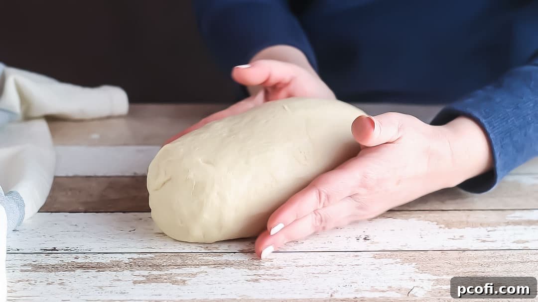 Hands gently shaping the white bread dough into an elongated loaf on a lightly floured surface, preparing it for the loaf pan.
