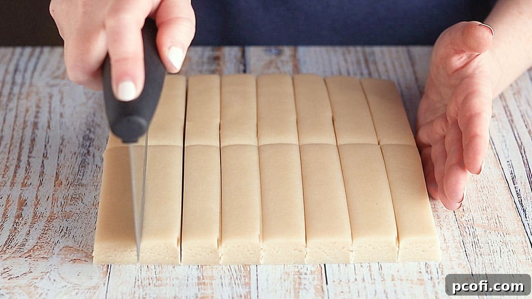 A baker precisely cutting chilled shortbread cookie dough into classic bar shapes on a surface.