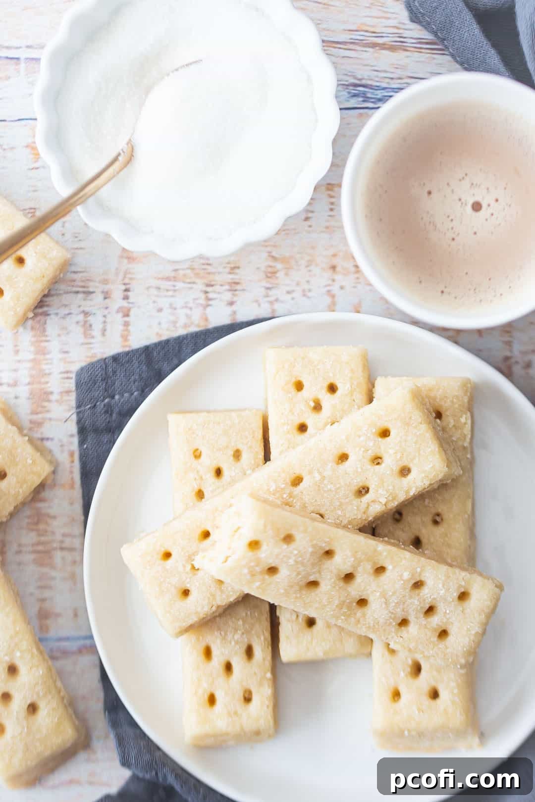 An overhead shot of festive shortbread cookies for Christmas, artfully arranged on a plate with a gray napkin and a steaming cup of tea, ready to be enjoyed.