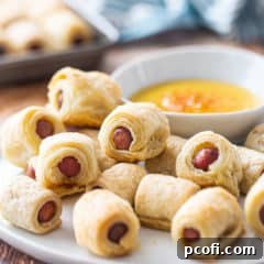 Pigs in a blanket on a plate with honey mustard dip.
