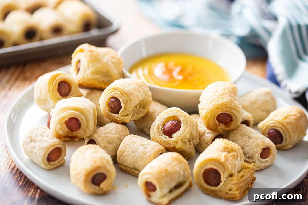 A beautifully arranged platter of homemade pigs in a blanket, accompanied by a small bowl of creamy honey mustard sauce, ready for serving.