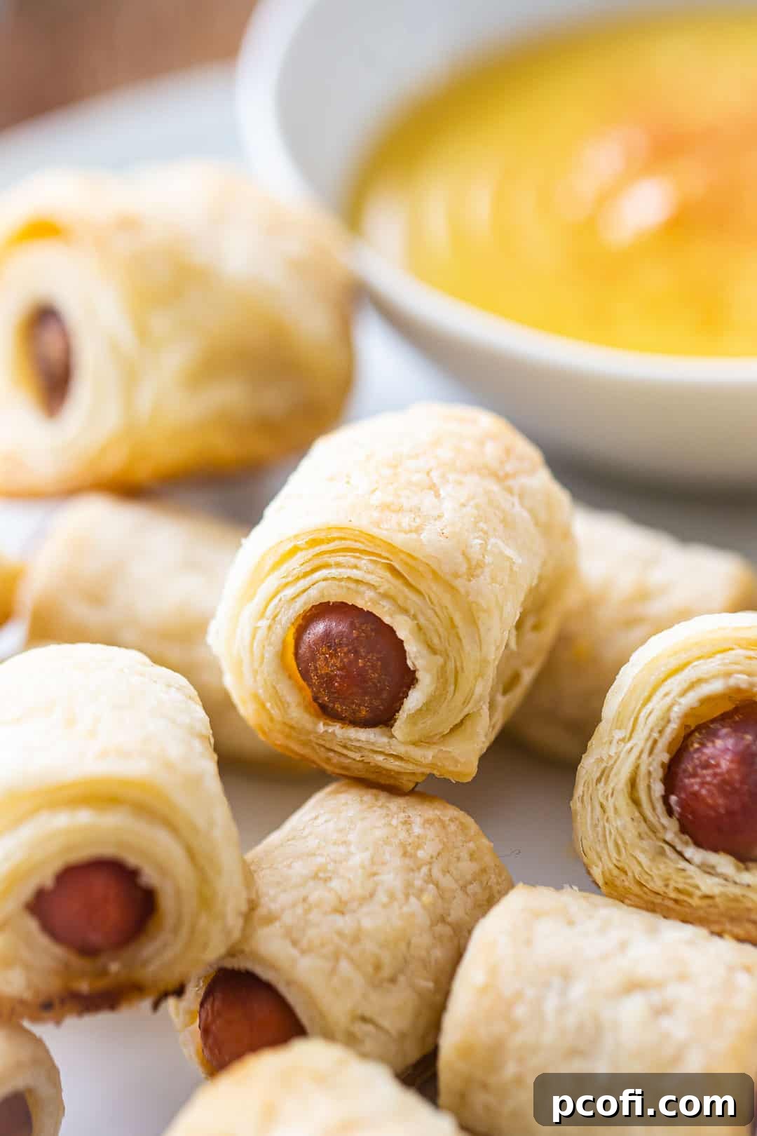 Detailed close-up of a single pig in a blanket, highlighting the many flaky layers of the golden homemade puff pastry.