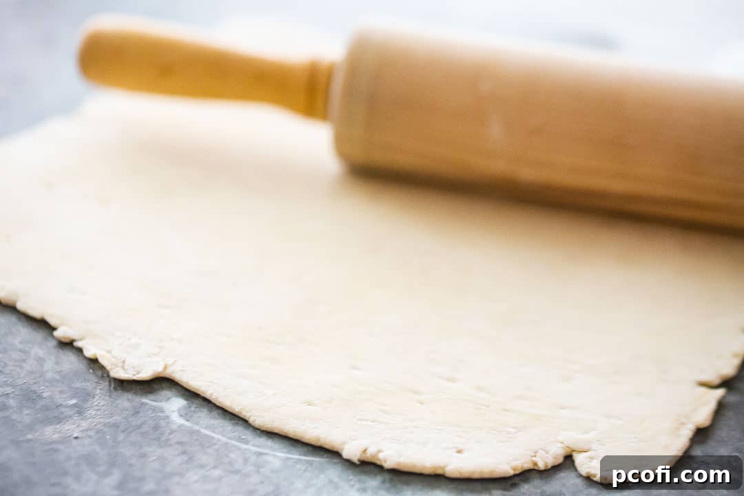 A rolling pin flattening puff pastry dough into a thin rectangle on a floured surface.