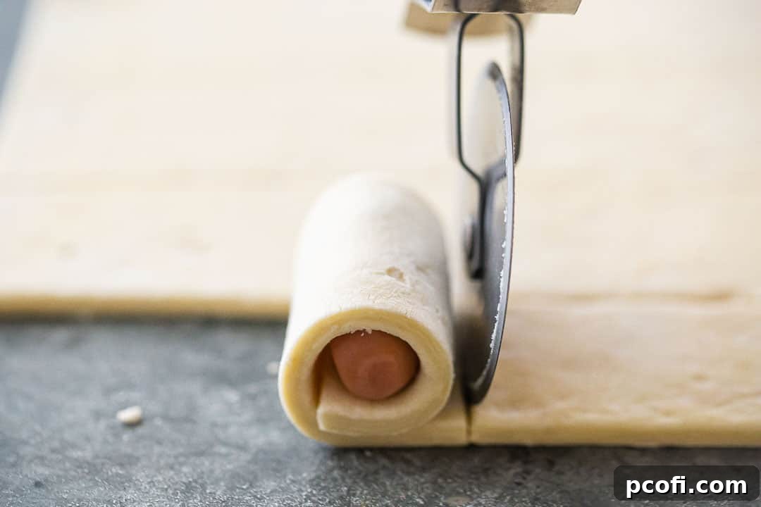 A mini hot dog being wrapped neatly in a strip of puff pastry.