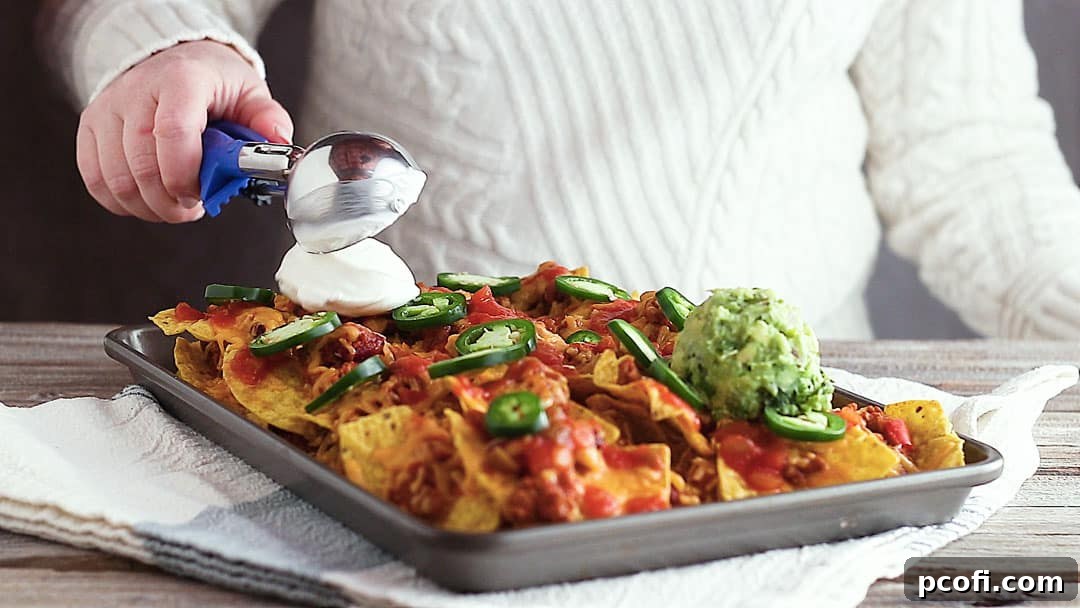 Topping sheet pan nachos with sour cream.