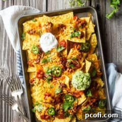 Overhead image of nachos on a sheet pan with forks and fresh cilantro.